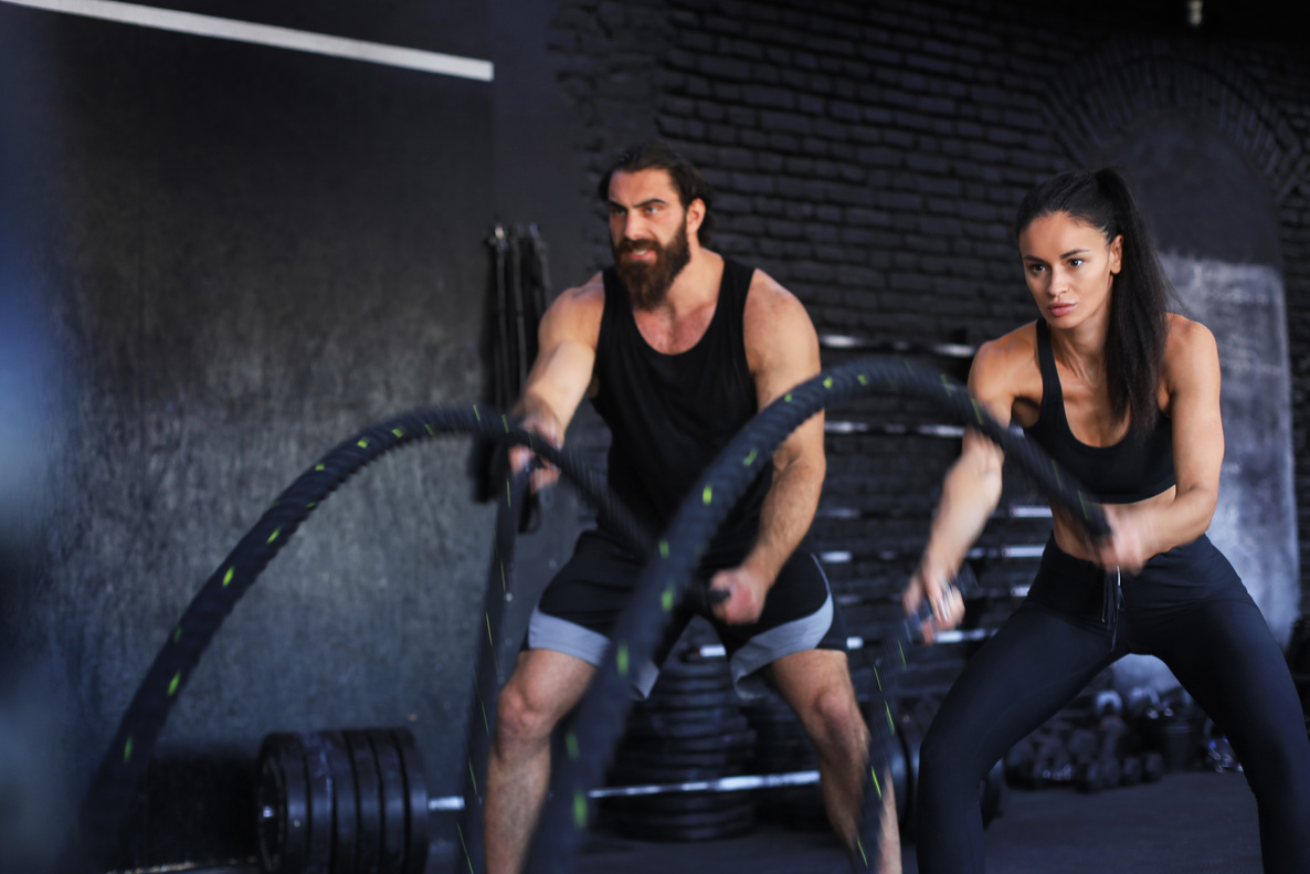 Athletic young couple with battle rope doing exercise in functional training fitness gym.